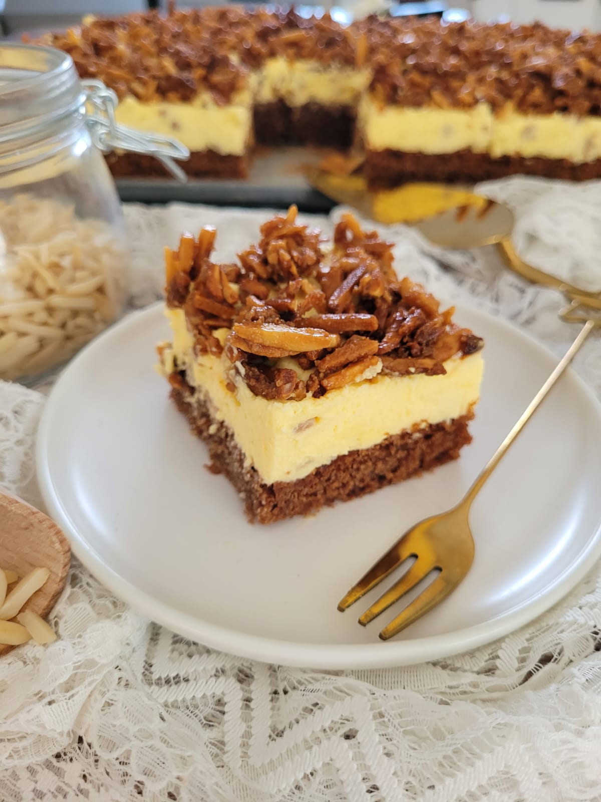 Bild eines Stücks Mandelkrokant-Kuchen mit dem Blech des restlichen Kuchens im Hintergrund